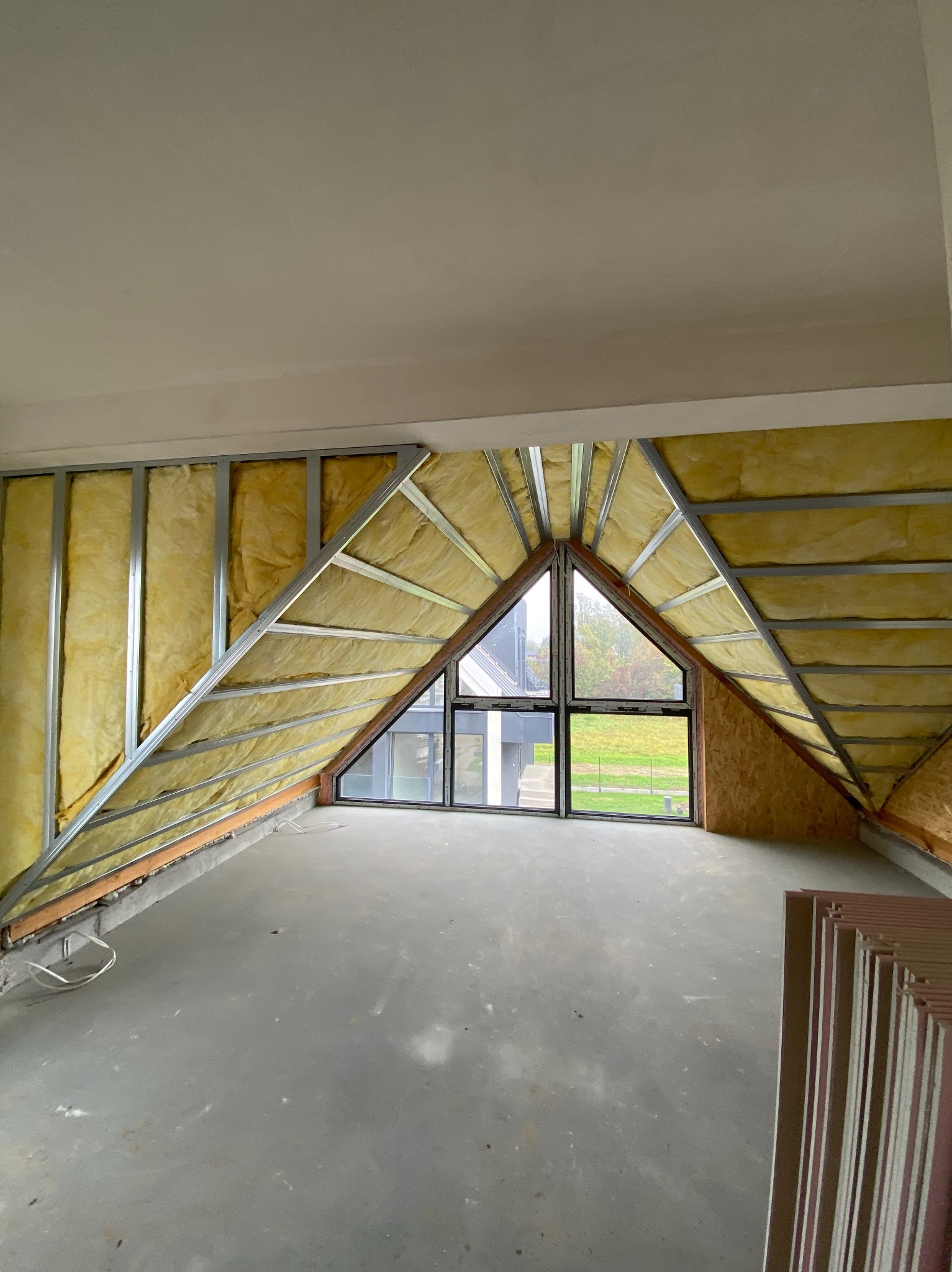 Poddasze z oknem w szczycie, ocieplone wełną mineralną, z metalową konstrukcją pod płyty karton-gips. Widoczne płyty czekające na montaż.