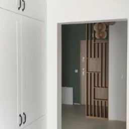 Wnętrze mieszkania z białymi szafami na ścianie, czarnymi uchwytami, widok na przedpokój z drewnianą ażurową ścianką działową i lampami w stylu boho.