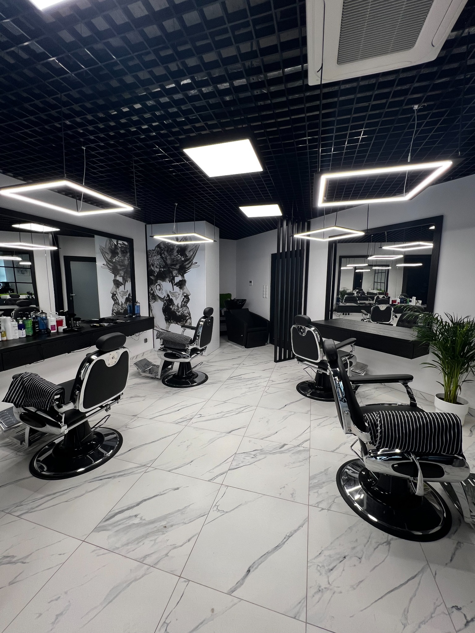 Nowoczesny salon fryzjerski z marmurową podłogą, czarnymi fotelami barberskimi, lustrami i kwadratowymi lampami sufitowymi.