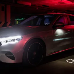 Srebrny Mercedes-Benz w garażu podziemnym w Ożarowie Mazowieckim, z podświetlanym logo na podłożu i czerwonym oświetleniem sufitowym.