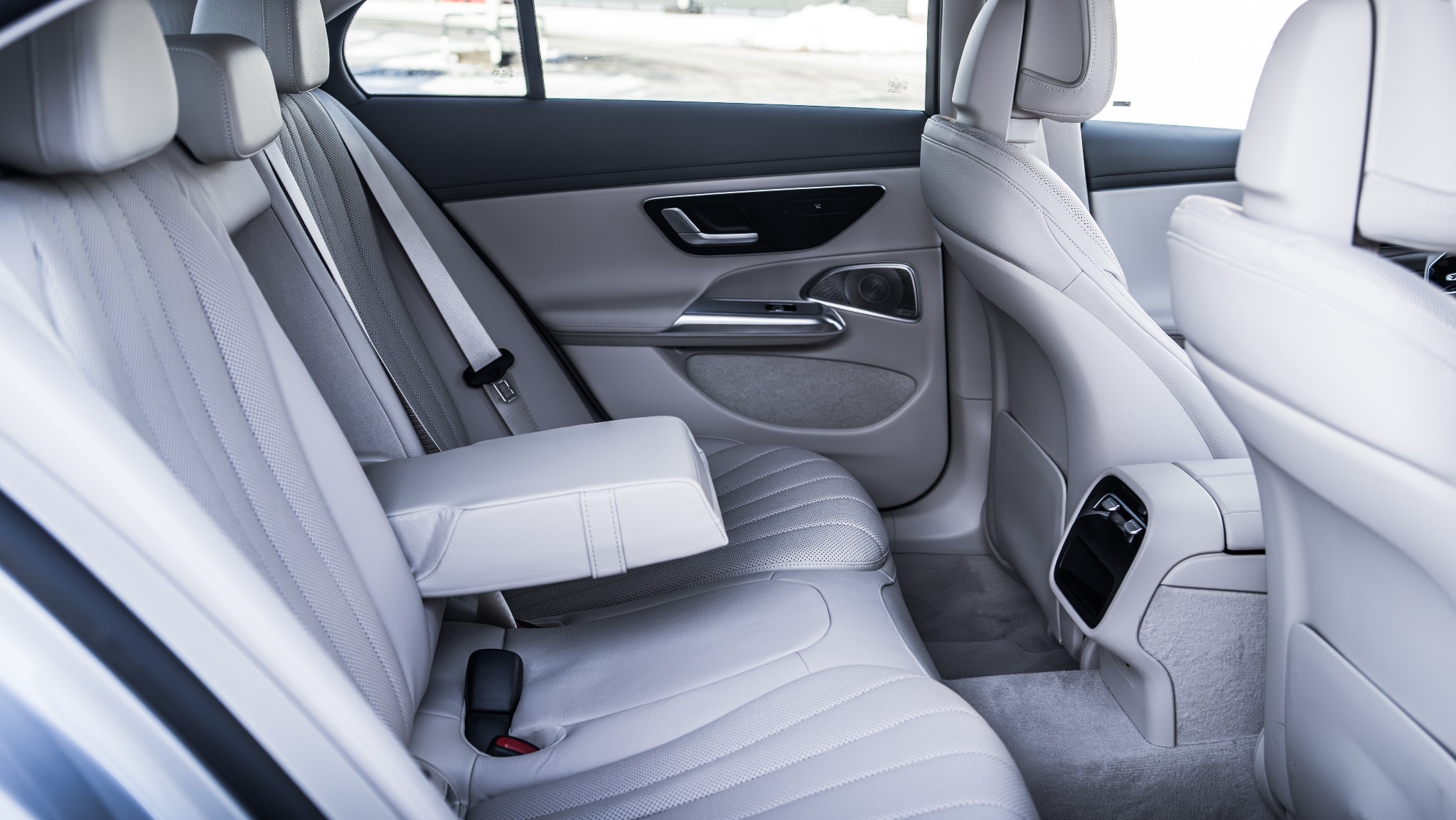 Wnętrze samochodu z jasną skórzaną tapicerką, widok na tylną kanapę z rozkładanym podłokietnikiem i pasami bezpieczeństwa.