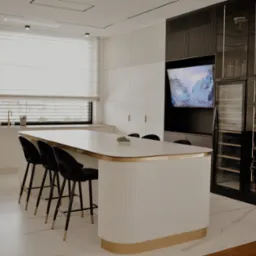 Elegancka kuchnia z wyspą, czarnymi hokerami i zabudową z barkiem. Białe fronty szafek, marmurowy blat, złote akcenty. Nowoczesny design z dbałością o detale.