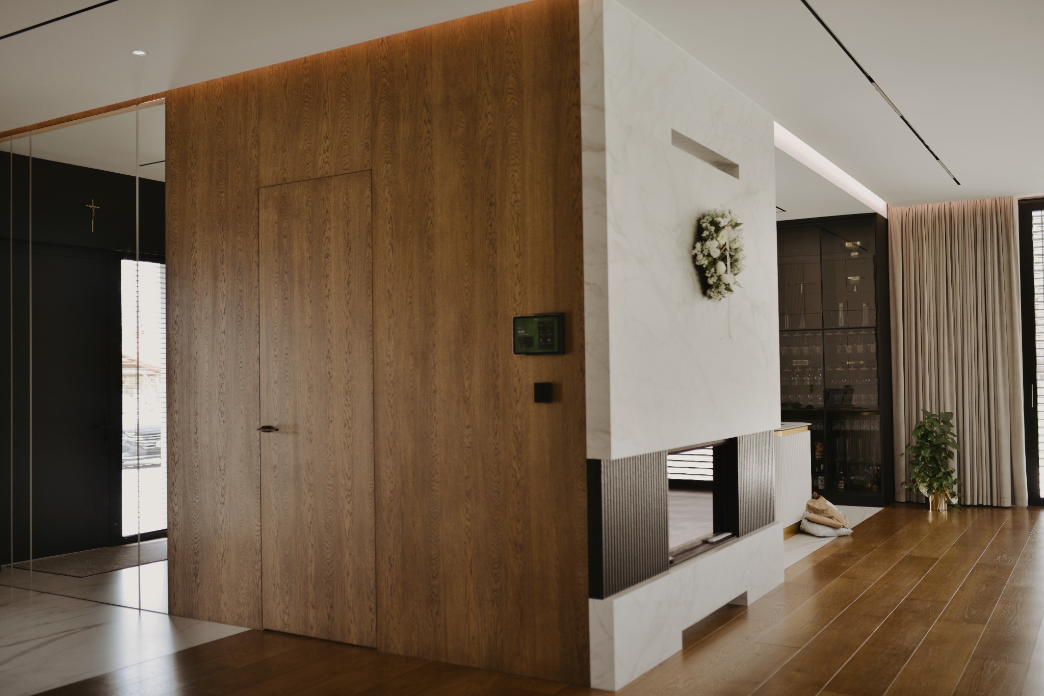 Nowoczesny salon z drewnianą ścianą z ukrytymi drzwiami, marmurowym kominkiem i dekoracją kwiatową. Minimalistyczny design z elementami drewna i kamienia.