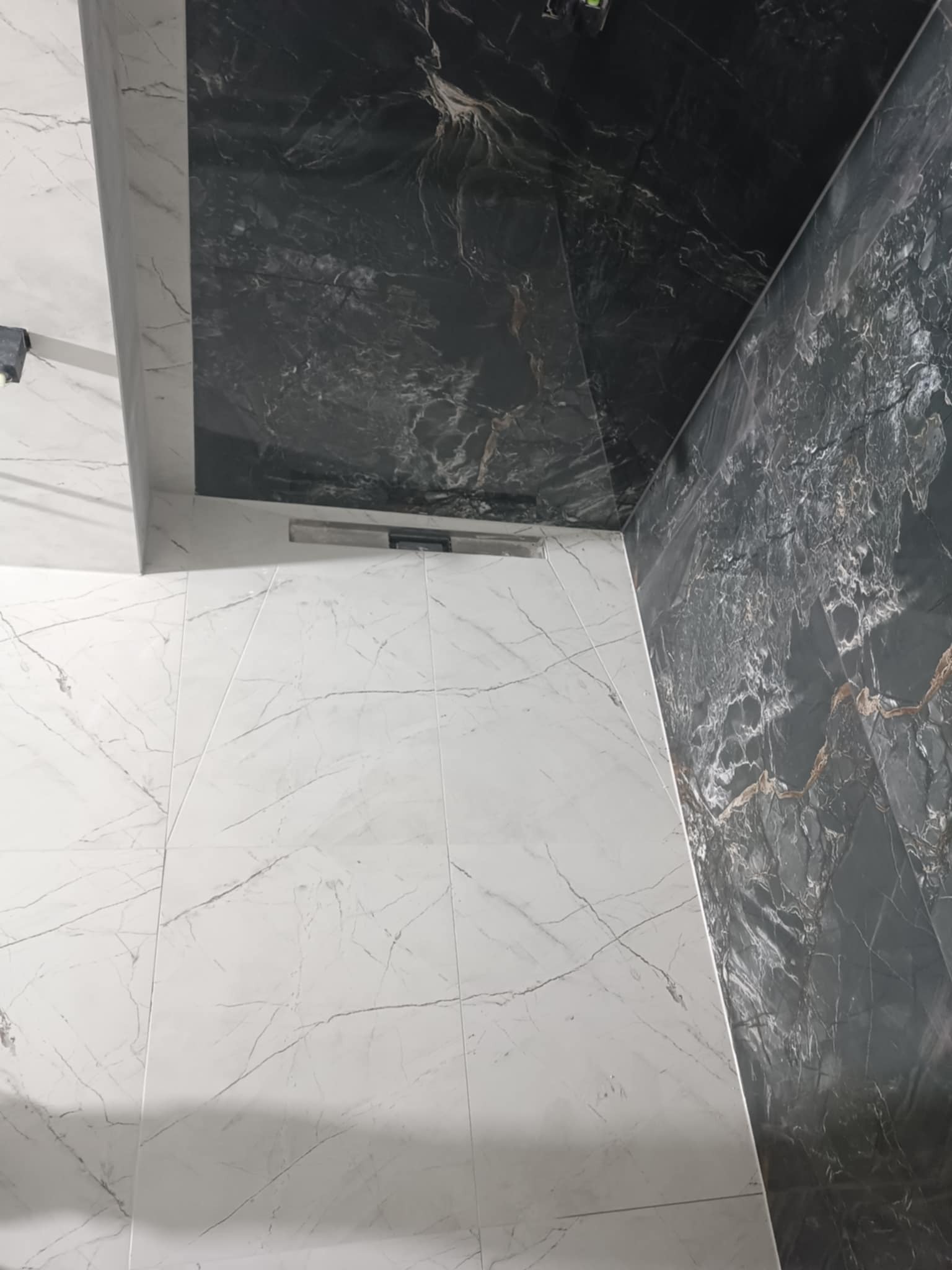 Wykończona łazienka z białymi i czarnymi marmurkowymi płytkami, widoczny odpływ liniowy w podłodze i kontrastowe połączenie kolorów.