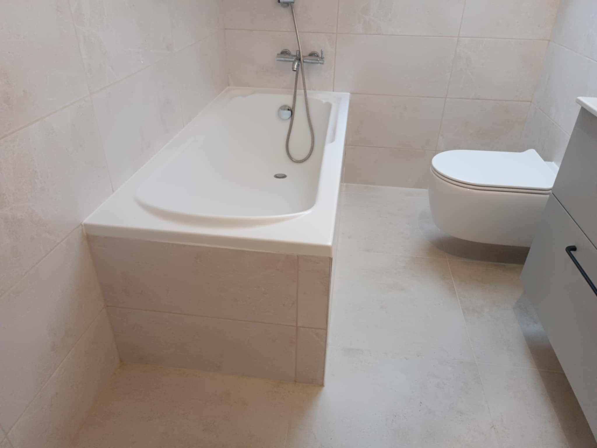 Jasna łazienka po remoncie w Lublinie: widok na wannę obudowaną płytkami, toaletę i fragment szafki pod umywalkę.