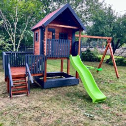 PURE WOOD Daniel Mojsa - Drewniany plac zabaw z domkiem, zjeżdżalnią i huśtawką na trawniku. Elementy pomalowane na brązowo i grafitowo. Widok z bliska, w tle drzewa i ogrodzenie.