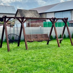 PURE WOOD Daniel Mojsa - Drewniana huśtawka ogrodowa z trzema siedziskami: ławka, pojedyncze siedzisko i okrągłe krzesło wiszące, na tle zielonego trawnika i budynków gospodarczych.