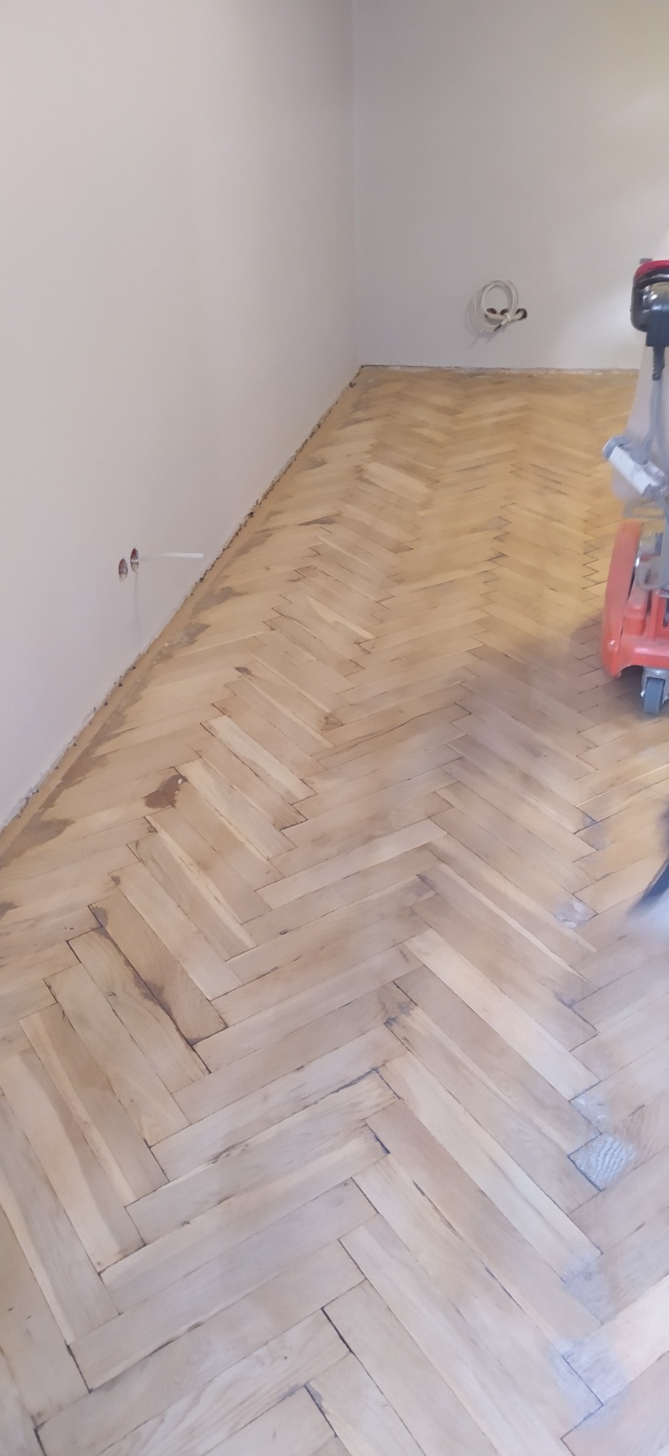 Parkiet ułożony w jodełkę, częściowo przeszlifowany maszyną, widoczne ślady po szlifowaniu i przygotowaniu do dalszej obróbki.