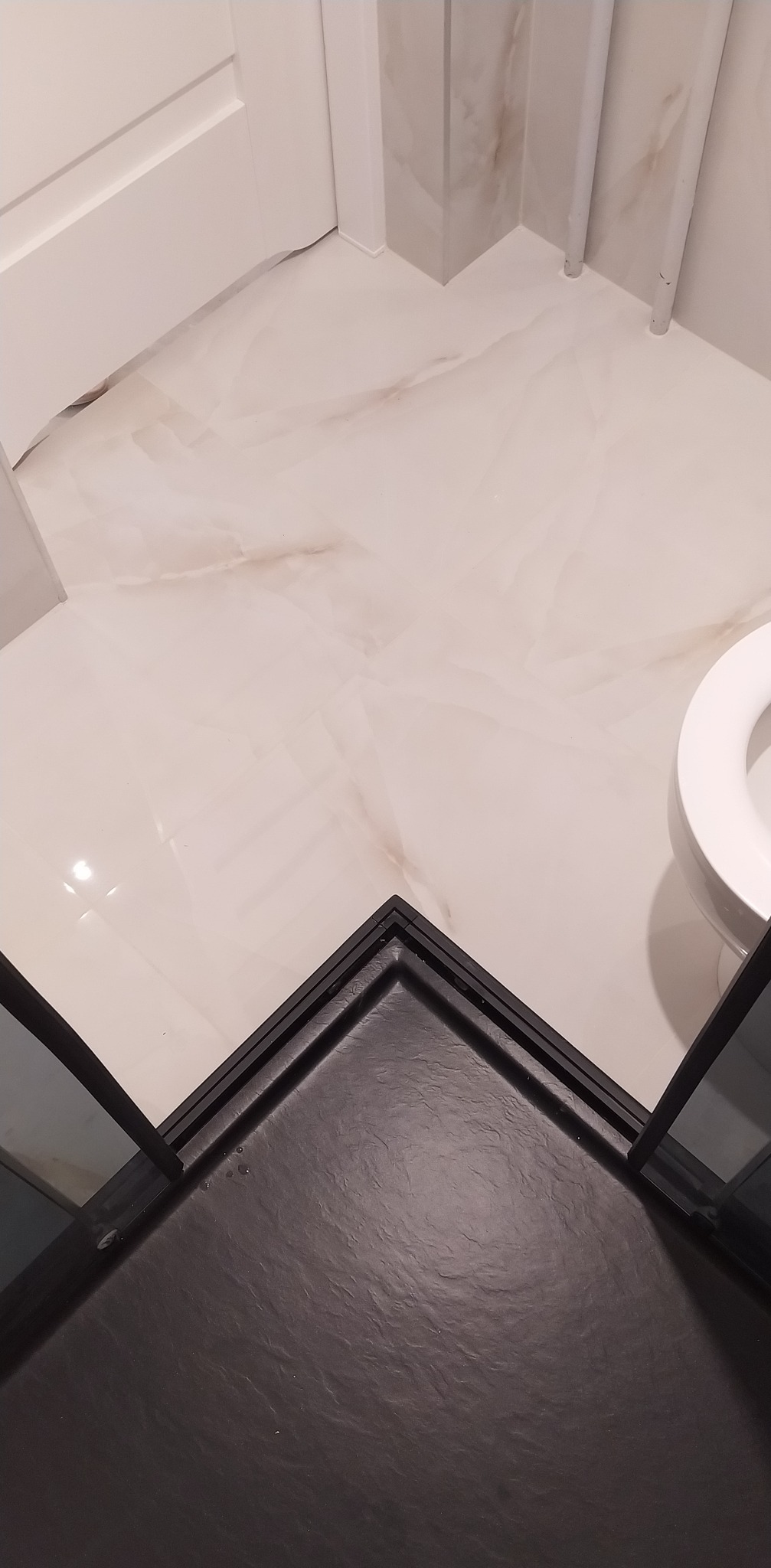 Czarny brodzik kabiny prysznicowej z widocznymi detalami wykończenia w łazience w Krakowie, z jasnymi, marmurkowymi płytkami podłogowymi i fragmentem toalety.