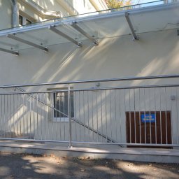 VERME SPÓŁKA Z OGRANICZONĄ ODPOWIEDZIALNOŚCIĄ - Zewnętrzna balustrada ze stali nierdzewnej przy schodach wejściowych do budynku, z przeszklonym daszkiem nad wejściem i tabliczką informacyjną na drzwiach.