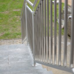 VERME SPÓŁKA Z OGRANICZONĄ ODPOWIEDZIALNOŚCIĄ - Nowoczesna balustrada metalowa ze stali nierdzewnej na schodach zewnętrznych z szarych płyt. Trawa i samochód w tle. Minimalistyczny design.
