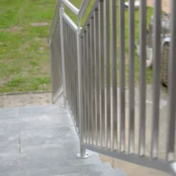 Nowoczesna balustrada metalowa ze stali nierdzewnej na schodach zewnętrznych z szarych płyt. Trawa i samochód w tle. Minimalistyczny design.