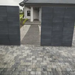 Nowoczesne ogrodzenie z szarej kostki betonowej i ścieżka z desek prowadząca do domu. Minimalistyczny design z dbałością o detale i symetrię.