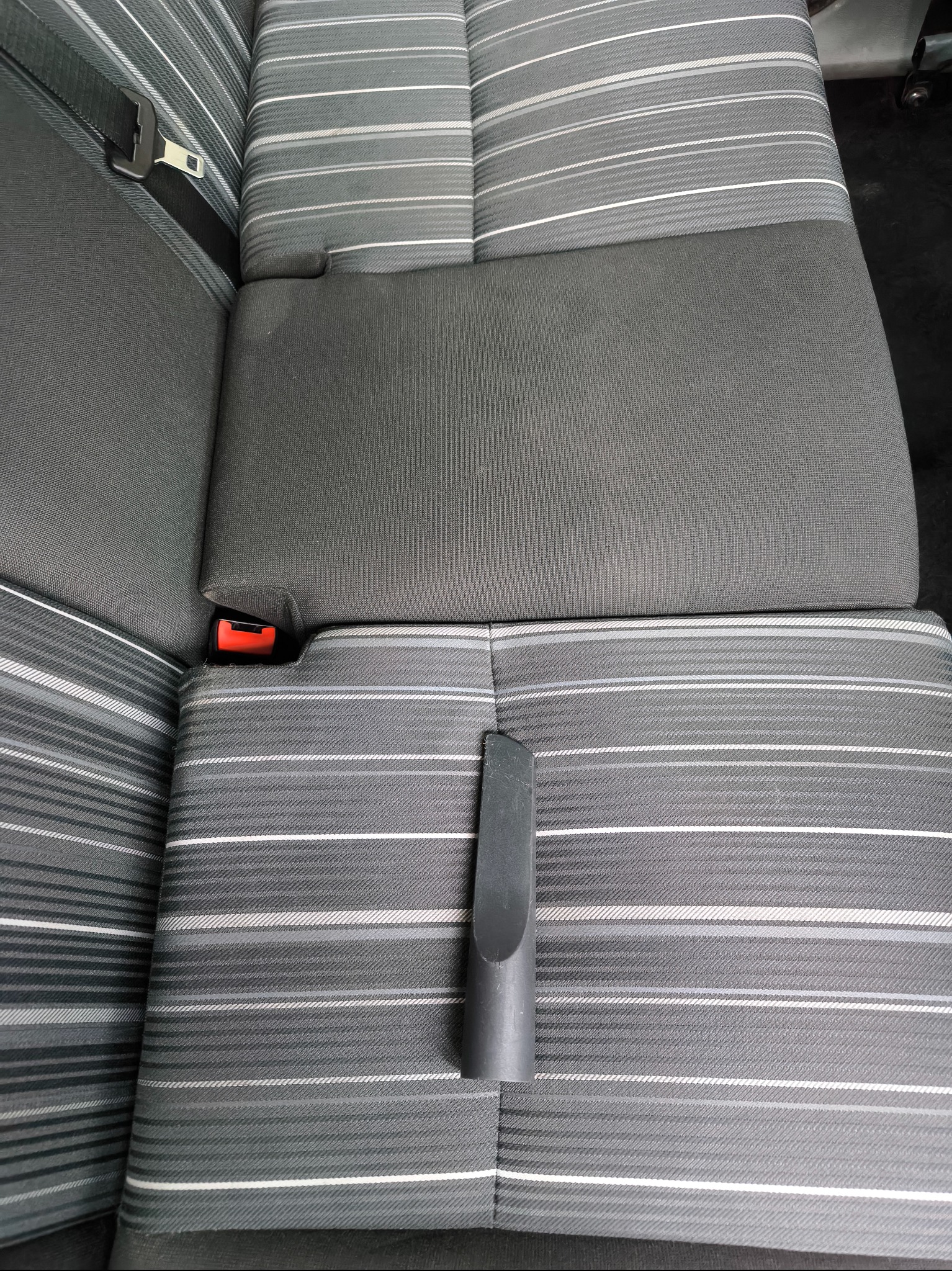 Dysza odkurzacza na szarej, prążkowanej tapicerce samochodowej. Widoczny fragment fotela z pasami bezpieczeństwa. Detal czyszczenia wnętrza pojazdu.