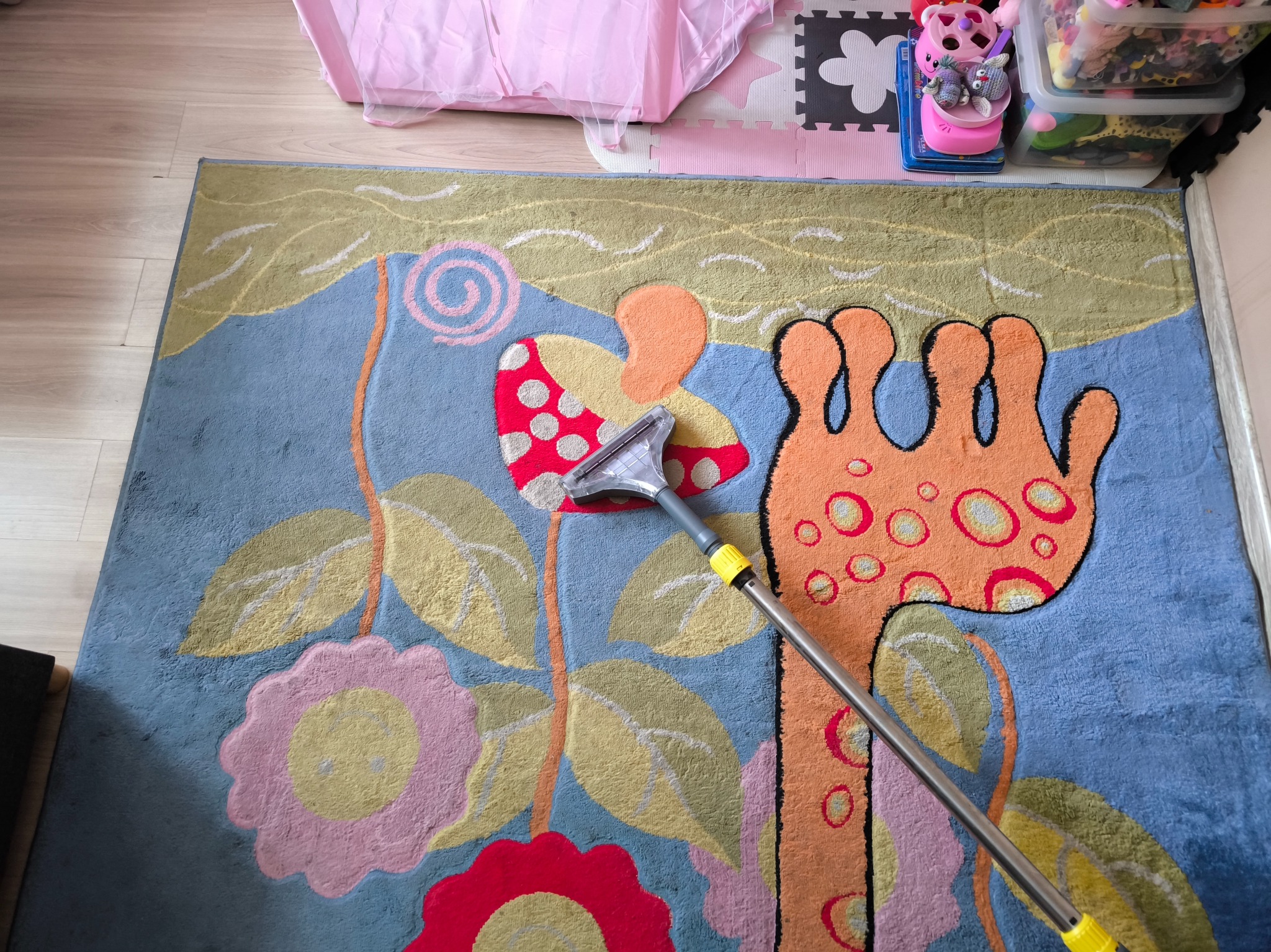 Kolorowy dywan z wzorem kwiatowym czyszczony odkurzaczem piorącym. Widoczne detale wzoru i dysza odkurzacza. Ujęcie z góry, oświetlenie naturalne.