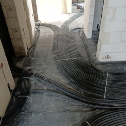 ELEKTRO-TECH DAMIAN GODLEWSKI - Kable elektryczne w peszlach ułożone na podłodze w surowym stanie budynku. Widoczne białe ściany z betonu komórkowego. Instalacja przed zalaniem wylewką.