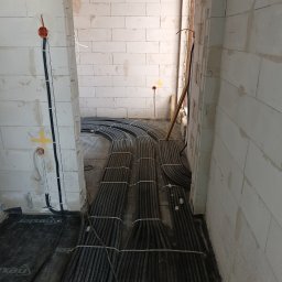 ELEKTRO-TECH DAMIAN GODLEWSKI - Kable elektryczne ułożone na podłodze w surowym wnętrzu, widoczne puszki instalacyjne na ścianie z betonu komórkowego. Etap prac instalacyjnych przed wylewką.