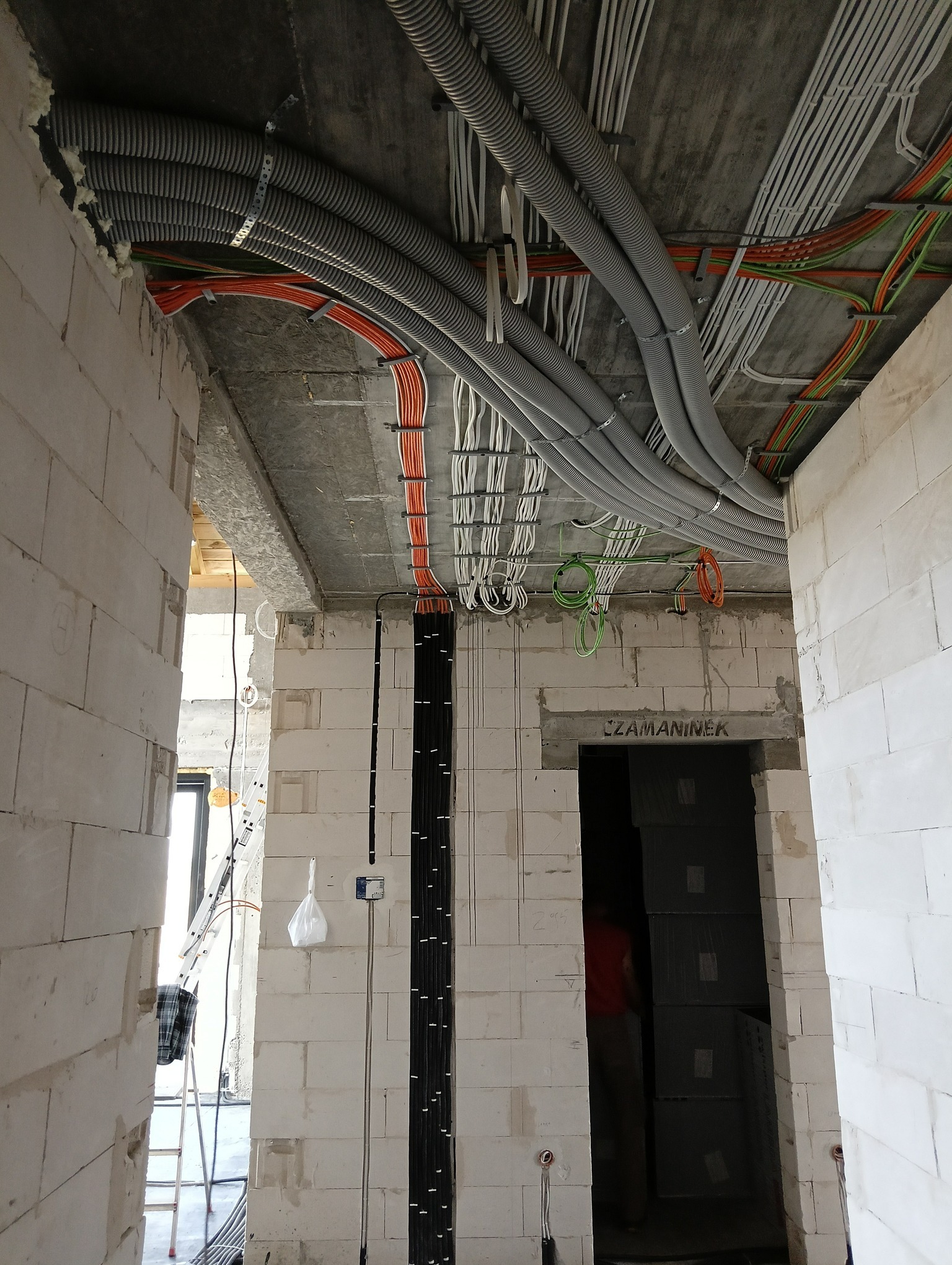 Wnętrze w trakcie budowy z widocznymi, poprowadzonymi pod sufitem instalacjami elektrycznymi w peszlach i kablami w ścianach z betonu komórkowego.
