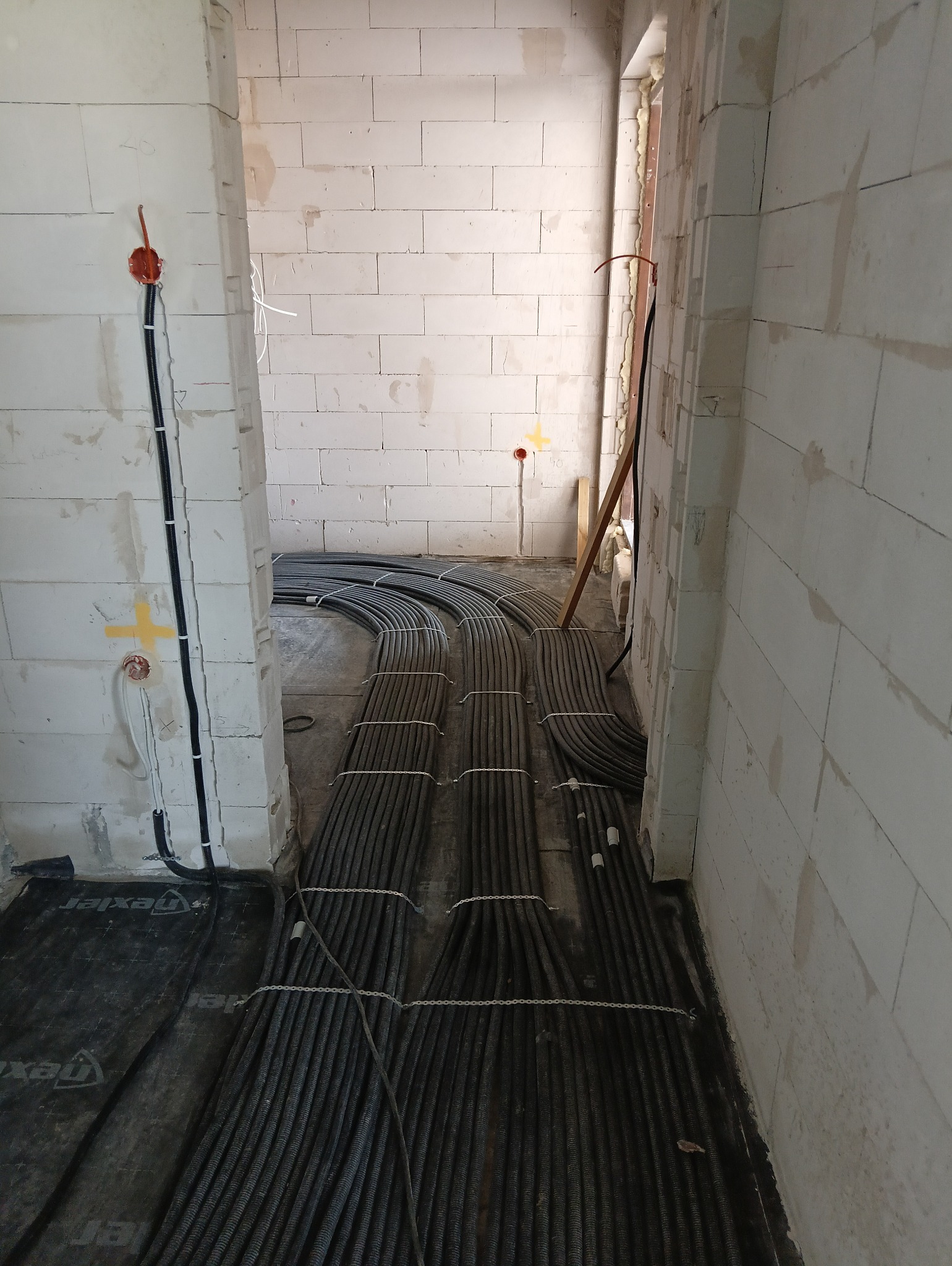 Kable elektryczne ułożone na podłodze w surowym wnętrzu, widoczne puszki instalacyjne na ścianie z betonu komórkowego. Etap prac instalacyjnych przed wylewką.