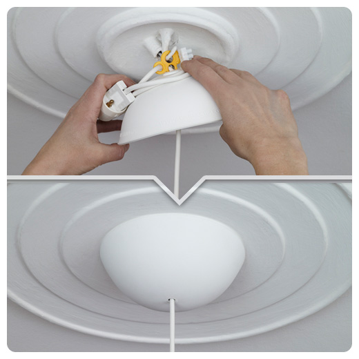 Instalacja lampy sufitowej CableCup: ręce montera mocują białą osłonę do sufitu z dekoracyjnymi okręgami, widoczne żółte złączki elektryczne.