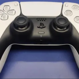 Biało-czarny kontroler do gier wideo leży na niebieskim tle, widoczne przyciski, analogi i logo.