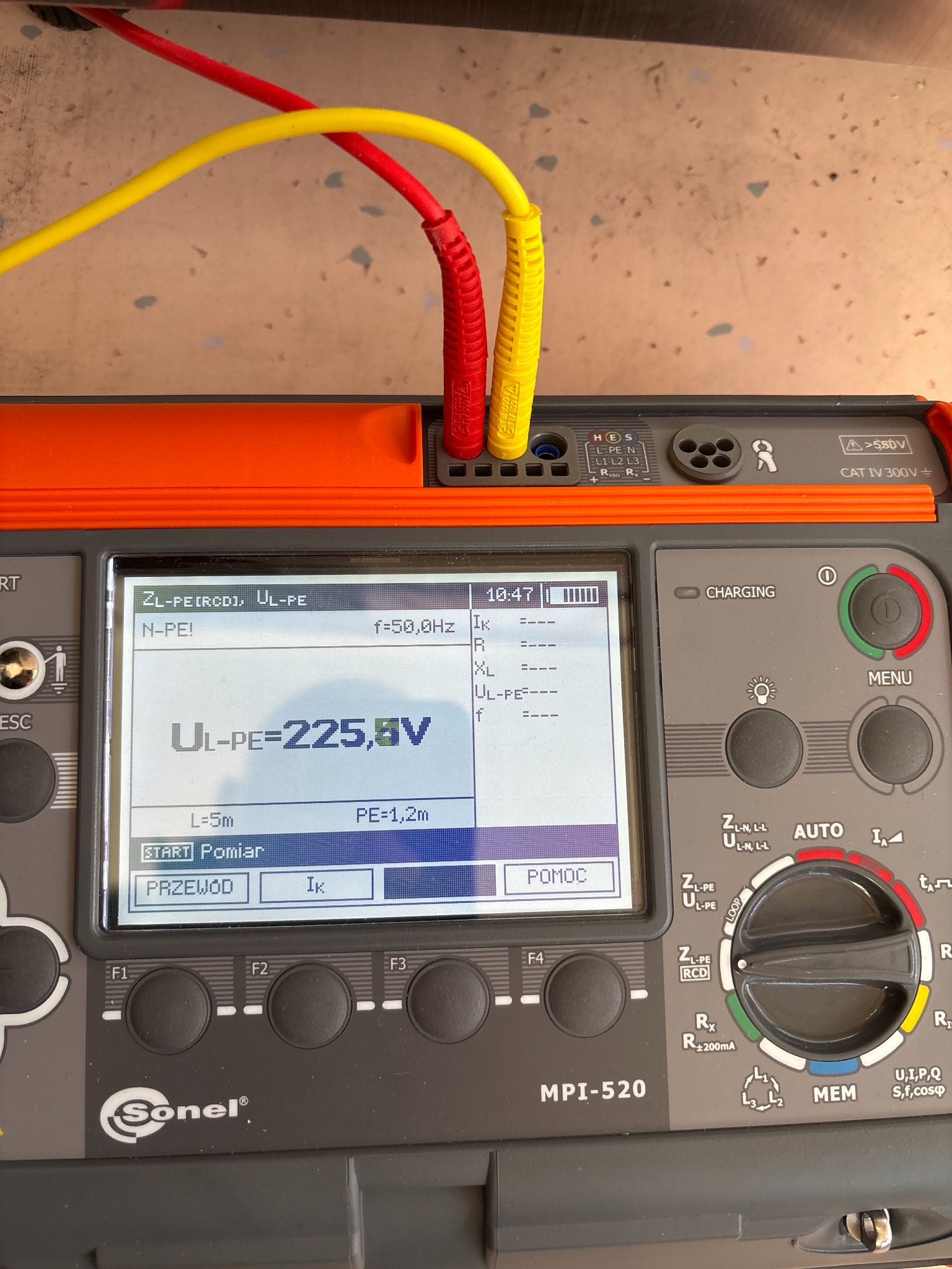 Miernik Sonel MPI-520 z podłączonymi przewodami pomiarowymi (czerwony i żółty) wyświetlający wynik pomiaru napięcia UL-PE = 225,8V na ekranie LCD.