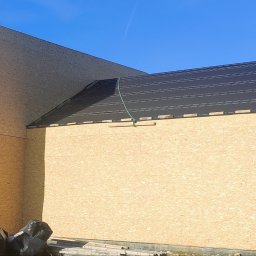 PrimeHome Oleksandr Prydvornyi - Surowy stan domu szkieletowego z płyt OSB, widoczne otwory okienne z drewnianym rusztowaniem i czarne pokrycie dachu z listwami kontrłat, worki ze śmieciami u podstawy ściany