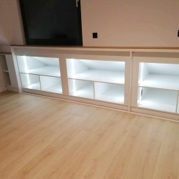P&J Meble - Biała szafa wnękowa pod skosem dachu z oświetleniem LED, drewniany blat, jasna podłoga. Minimalistyczny design.