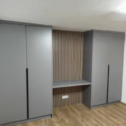 Szara szafa wnękowa z biurkiem i drewnianymi lamelami na ścianie, widok na podłogę z paneli. Minimalistyczny design, nowoczesne wykończenie.