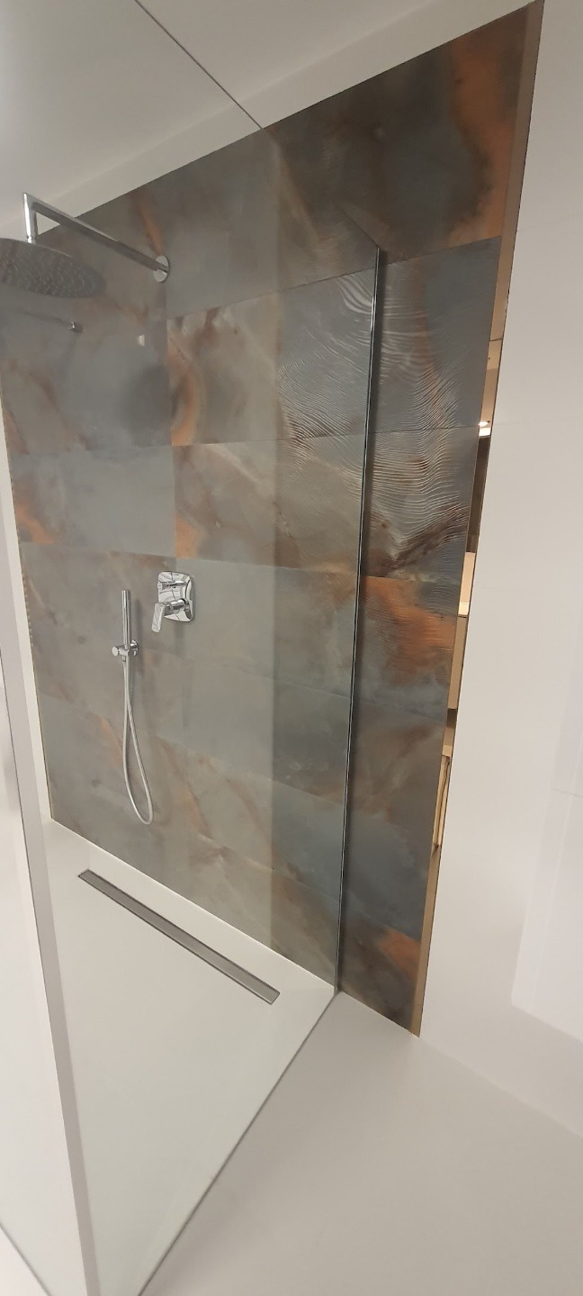 Nowoczesna kabina prysznicowa z panelami imitującymi marmur w odcieniach szarości i brązu, armatura chromowana, odpływ liniowy w posadzce.