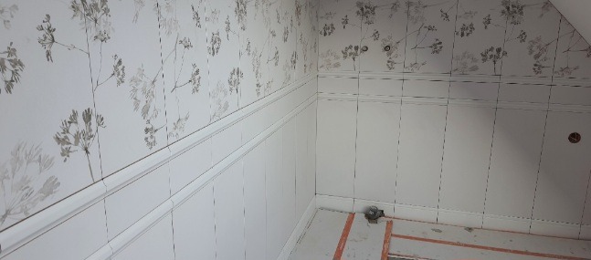 Ściany w pokoju wykończone panelami ściennymi z białymi listwami dekoracyjnymi i tapetą w kwiatowy wzór, widoczne przygotowania do dalszych prac wykończeniowych.