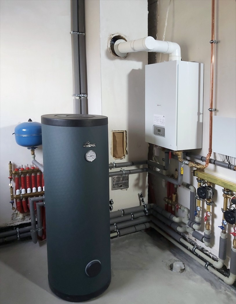 Kospel: Nowoczesny, szary zasobnik ciepłej wody użytkowej z kotłem gazowym na ścianie i rozbudowaną instalacją hydrauliczną w pomieszczeniu technicznym.