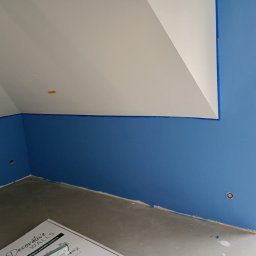 mitrahome serwis spółka cywilna Dorota Garczyńska Agnieszka Knapek - Pomalowane na niebiesko poddasze z białym sufitem, zabezpieczone taśmą malarską przy oknie. Częściowo widoczne panele dekoracyjne. Widok na zewnątrz przez okno.