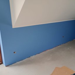 mitrahome serwis spółka cywilna Dorota Garczyńska Agnieszka Knapek - Pomieszczenie po malowaniu ścian na niebiesko, widoczne gładkie powierzchnie i przygotowane otwory na gniazdka, sufit biały, okno z widokiem na zewnątrz.