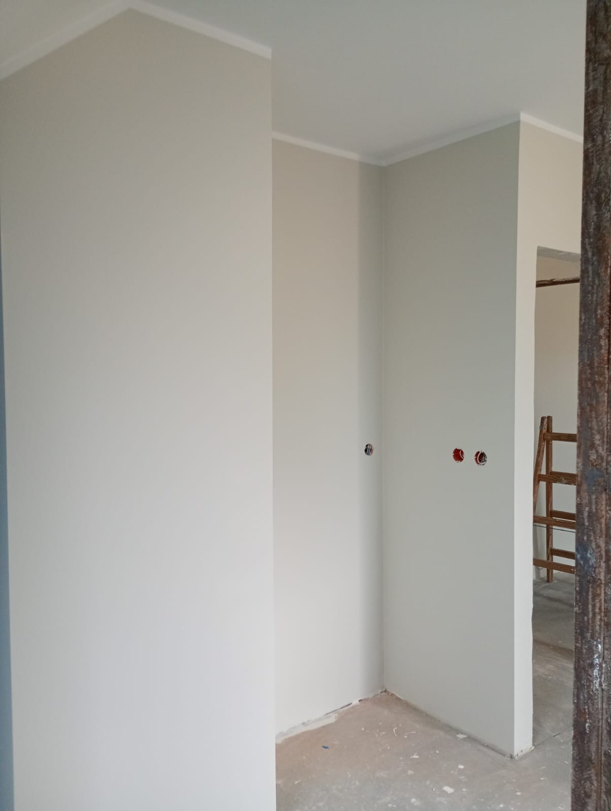 Jasne, świeżo pomalowane wnętrze z listwami przypodłogowymi i gniazdkami. W tle widoczna drabina, co sugeruje trwające prace wykończeniowe.