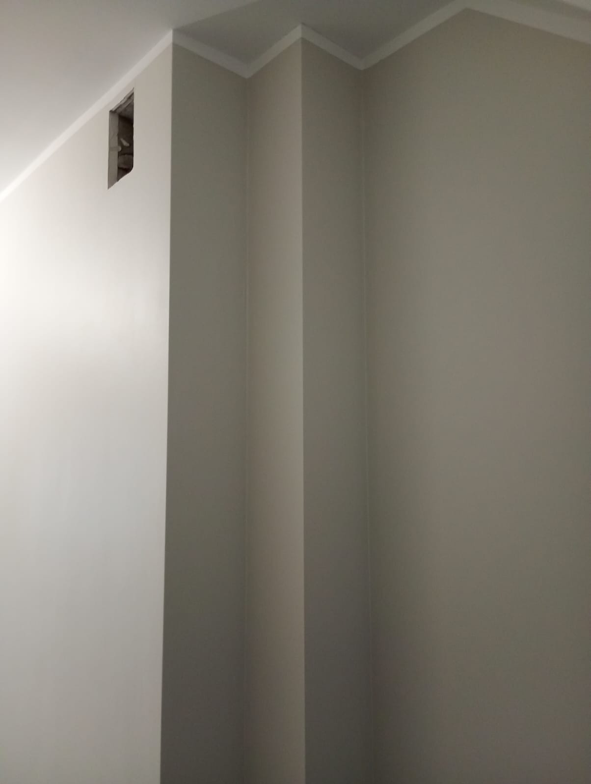 Świeżo pomalowane, beżowe ściany z dekoracyjną listwą przysufitową. Widoczny otwór w ścianie, prawdopodobnie po instalacji elektrycznej.