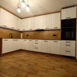 Nowoczesna kuchnia z białymi, lakierowanymi frontami, drewnianym blatem i podświetleniem LED, uzupełniona o czarne akcenty w postaci baterii i uchwytów.