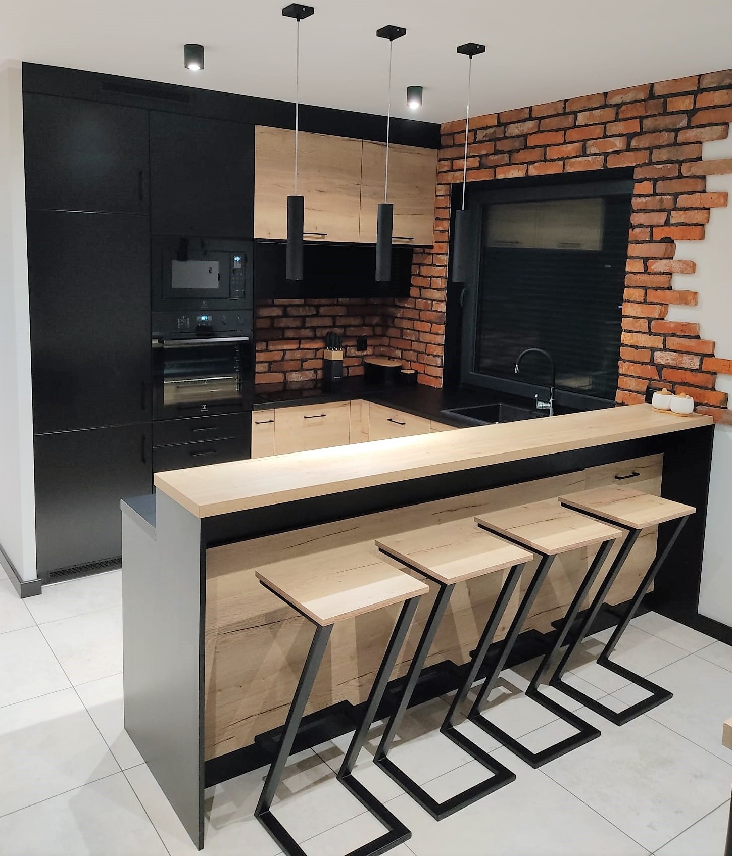 Nowoczesna kuchnia z czarnymi i drewnianymi szafkami, ceglaną ścianą i wyspą z hokerami o metalowych nogach w kształcie litery Z.