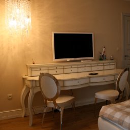 Dagi Studio - Biała toaletka z telewizorem, krzesłami i kryształowym żyrandolem w sypialni.