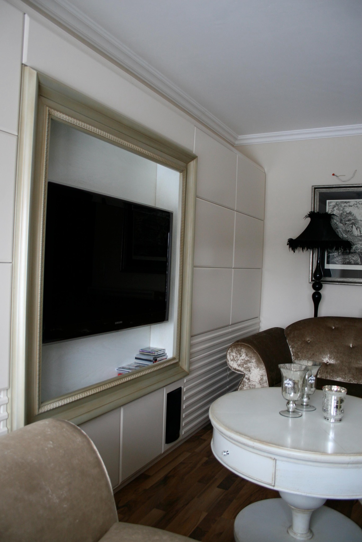 Salon z telewizorem w ozdobnej ramie, okrągłym stolikiem z srebrnymi świecznikami i lampą z frędzlami