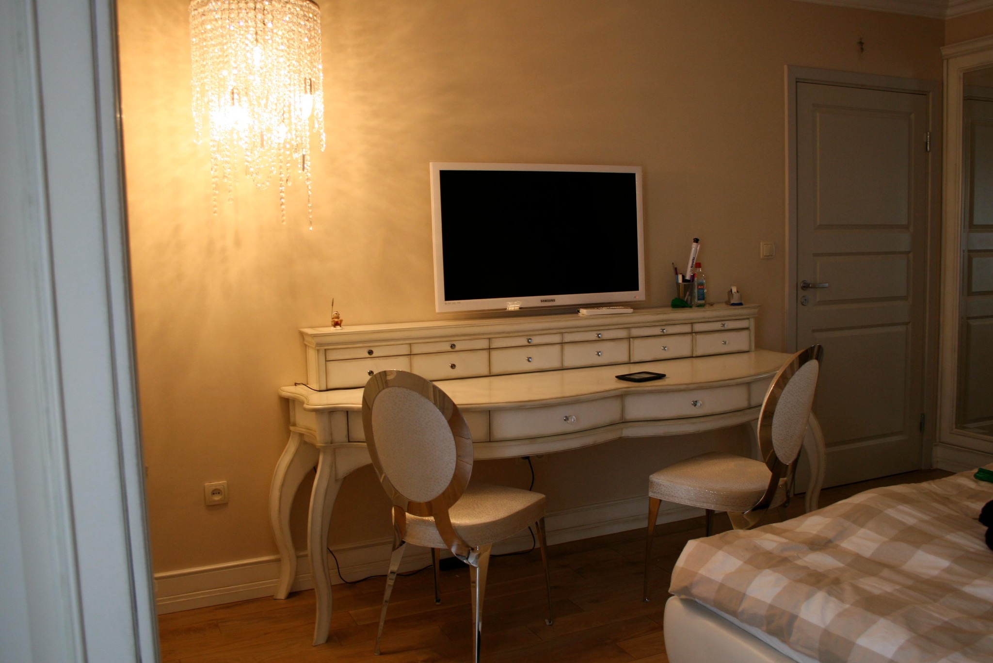 Biała toaletka z telewizorem, krzesłami i kryształowym żyrandolem w sypialni.
