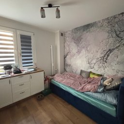 AD-BUD Adrian Wcisło - Pokój z łóżkiem, szafką i fototapetą z motywem kwitnących drzew. Świeżo położona fototapeta na ścianie za łóżkiem.