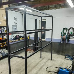 AD-BUD Adrian Wcisło - Spawana metalowa konstrukcja regału z profili zamkniętych, widoczna spawarka Sherman, warsztatowe otoczenie z narzędziami i akcesoriami.
