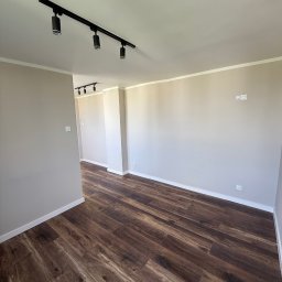 SERHII HULIAVSKYI sh.remontpro - Wykończone wnętrze: brązowe panele podłogowe, beżowe ściany z białymi listwami, czarne oświetlenie szynowe. Widok na sąsiednie pomieszczenie.