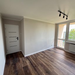 SERHII HULIAVSKYI sh.remontpro - Jasne, odświeżone wnętrze po remoncie: ciemne panele podłogowe, kremowe ściany, białe drzwi z czarnymi akcentami i okno balkonowe z widokiem na zieleń.