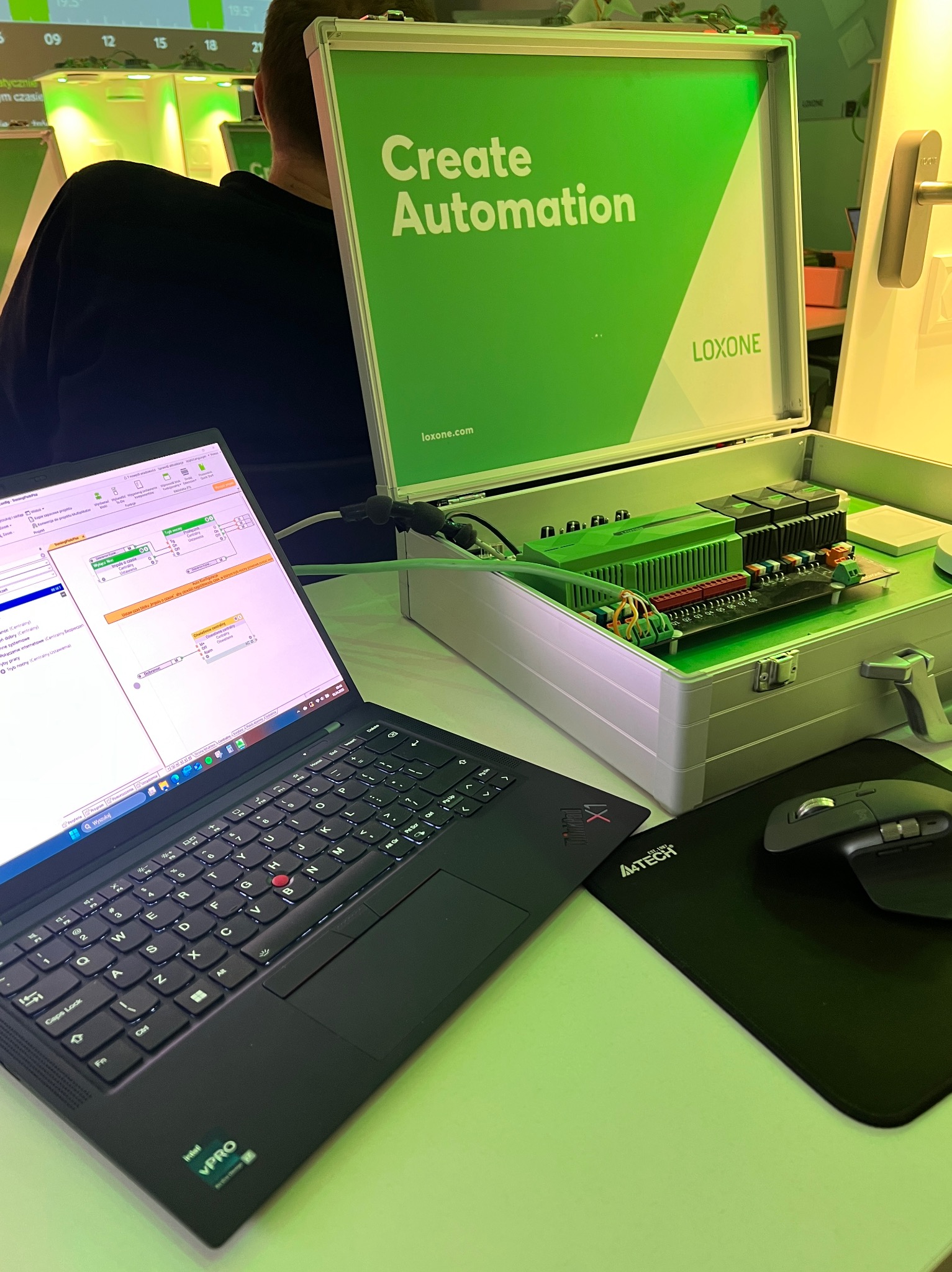 Konfiguracja systemu automatyki domowej Loxone na laptopie, obok otwarty panel sterowania w metalowej walizce. Widoczny interfejs oprogramowania.
