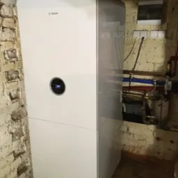 Nowoczesny piec gazowy marki Bosch, zainstalowany w piwnicy w Bierzglinku. Widoczne przyłącza i instalacja elektryczna na tle ceglanej ściany.