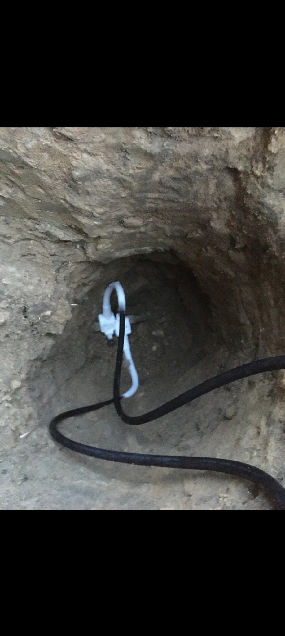 Studnia z wystającymi kablami i rurkami, w surowym, ziemistym otoczeniu. Widoczne przewody instalacyjne w trakcie prac ziemnych.