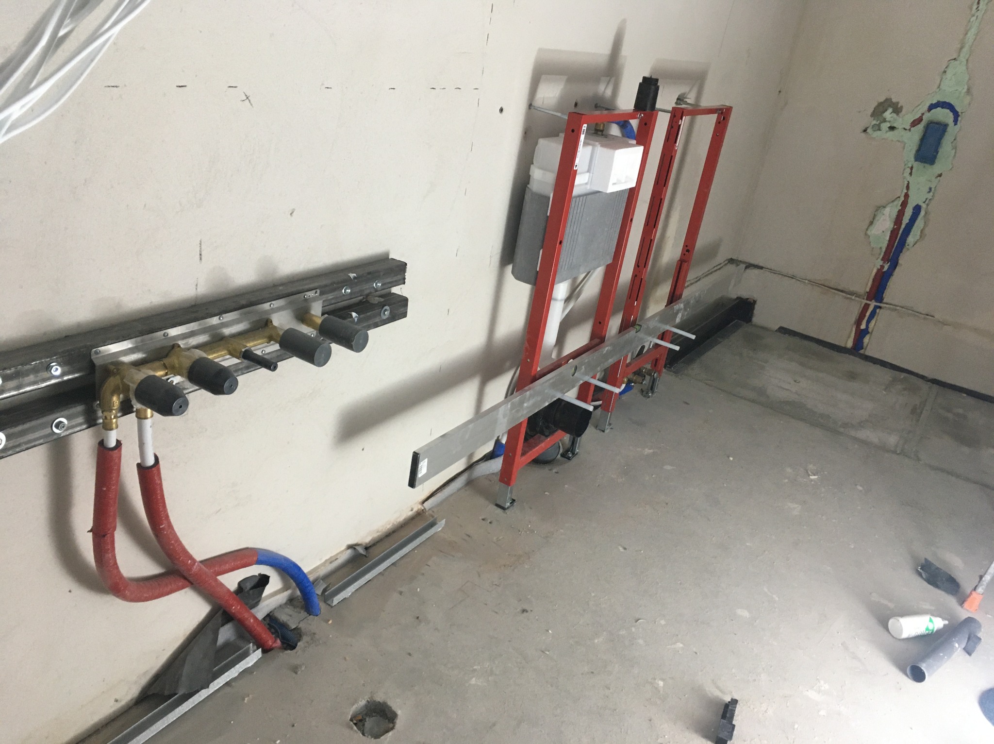 Montaż stelaża podtynkowego WC z widocznymi rurami doprowadzającymi wodę i odpływowymi w surowym wnętrzu. Instalacja hydrauliczna na etapie prac wykończeniowych.