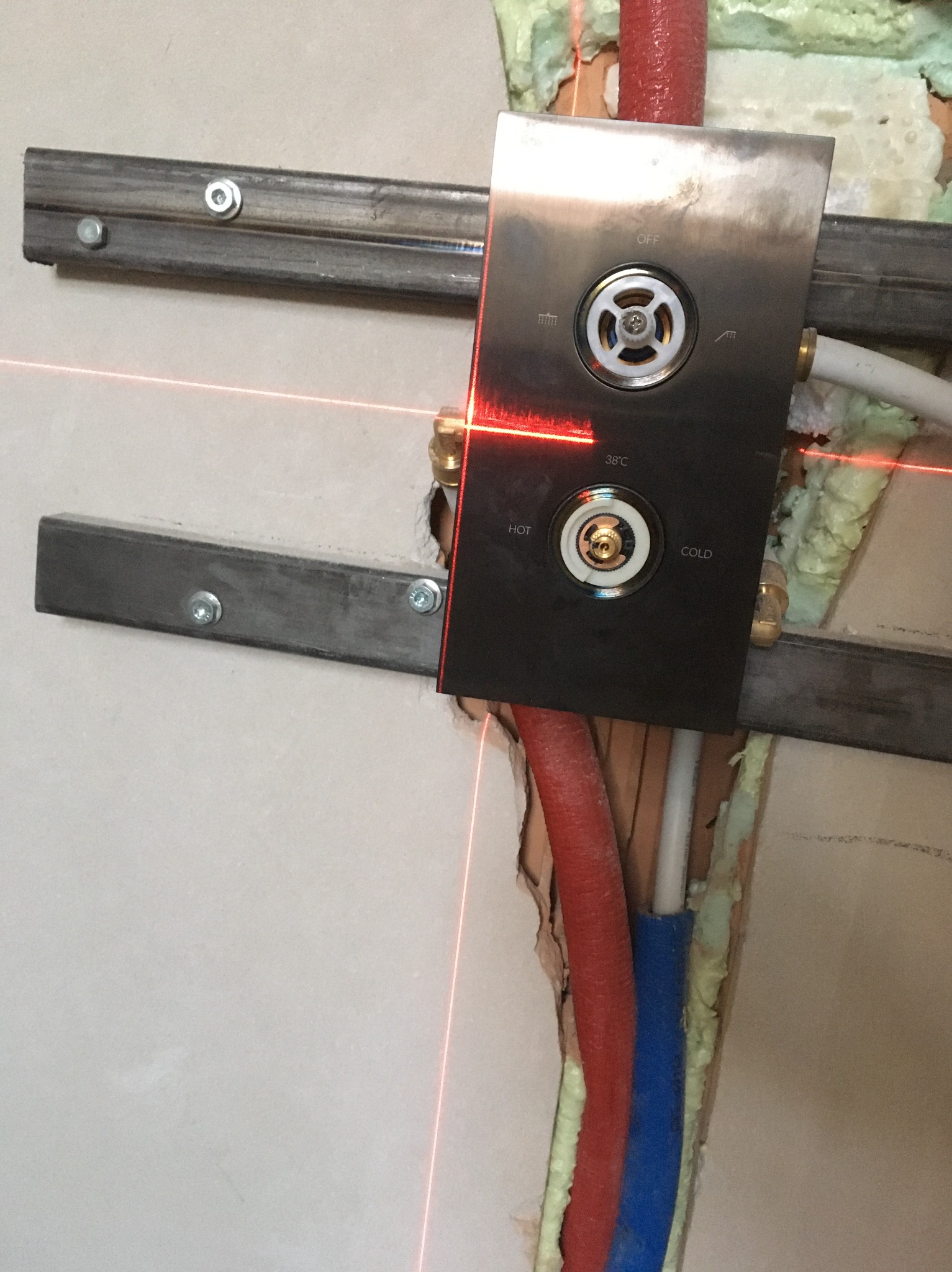 Metalowa płyta z pokrętłami ciepłej/zimnej wody, montowana na ścianie z widocznymi rurami i pianką montażową, poziomowana laserowo.